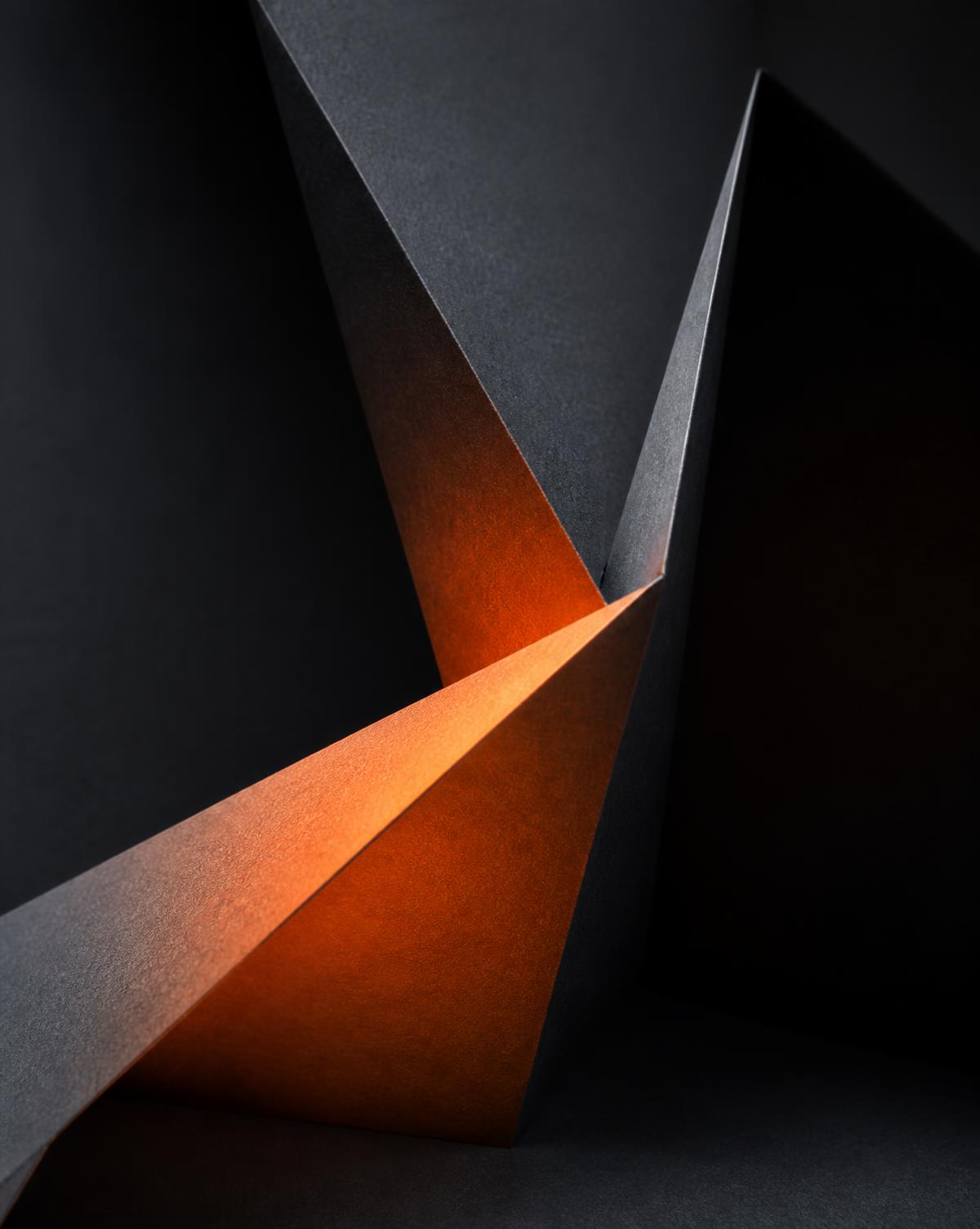 Folded specialty paper forming sharp angular planes lit with warm ember light